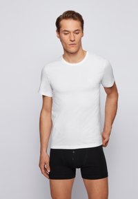Witte katoenen T-shirt met korte mouwen en een ronde hals, gecombineerd met zwarte boxershorts met twee knopen aan de voorkant.