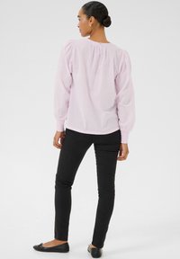 Blouse rose clair avec des pois, manches bouffantes et poignets élastiques, associée à un jean noir ajusté et des chaussures noires plates.