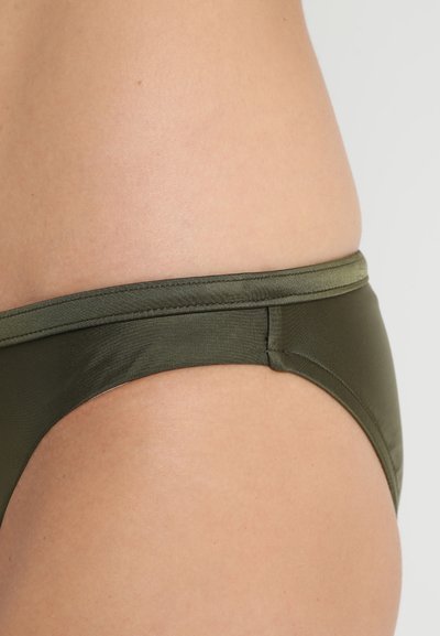 Λαδί μπικίνι κάτω μέρος σε λεία ύφανση με χαμηλή εφαρμογή και ελαστική μέση. Ασύρματα ραφές στα πλάγια για ελάχιστη ορατότητα.