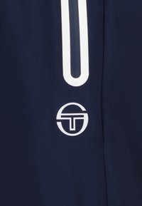 Donker marineblauwe sportbroek met een wit logo en een contrasterende witte accentstrip aan één kant. Gemaakt van glad, lichtgewicht materiaal.