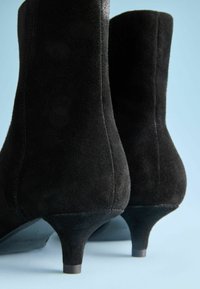 Čierne semišové členkové topánky s elegantným dizajnom, zužujúcim tvarom a 5 cm podpätkom. Majú hladkú textúru a minimálne steh.