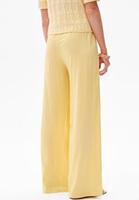 Lichtgele wijde broek van soepel stof, met een elastische tailleband en een vloeiende silhouet.