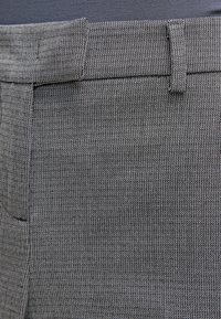 Grått texturerat tyg med ribbat mönster, med en rak midja och bälteshällor, som visar subtila färgvariationer.