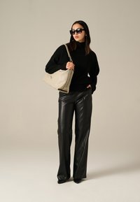 Maglione oversize nero a maglia, pantaloni larghi in finta pelle, borsa beige con logo impresso, occhiali da sole neri, vestibilità elegante, texture lisce.