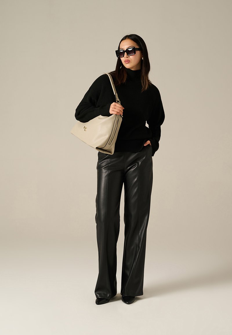 Maglione oversize nero a maglia, pantaloni larghi in finta pelle, borsa beige con logo impresso, occhiali da sole neri, vestibilità elegante, texture lisce.