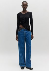 Schwarzes Langarmtop mit Wickeldesign, kombiniert mit blauen Jeans im weit geschnittenen Stil. Flache schwarze Schuhe runden das Outfit ab. Sanfte Texturen.