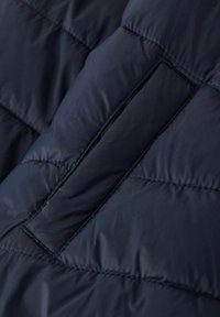Primer plano de una chaqueta acolchada azul marino con textura de acolchado, que presenta un diseño de costura horizontal y un bolsillo discreto con un acabado de borde limpio.