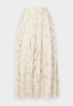 Longue jupe crème avec un motif floral subtil et des détails à volants en cascade, fabriquée en tissu léger et transparent.