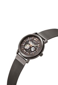 Montre avec bracelet en maille noire et boîtier rond. Présente un cadran sombre texturé, des accents en or rose et un design squelettique ouvert affichant les mécaniques internes.