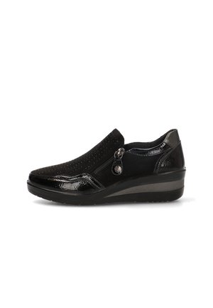 Zapato negro tipo slip-on con tacón cuña, empeine perforado, detalles brillantes en la puntera y el talón, y cremallera lateral con tirador decorativo.
