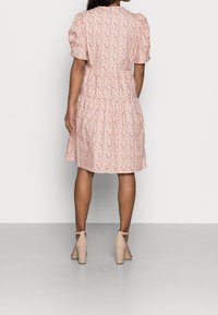 Rosa blommig klänning med korta puffärmar, åtstramad midja och lagerfördelad kjol. Buren med beige högklackade skor med ankelrem, slät textur.