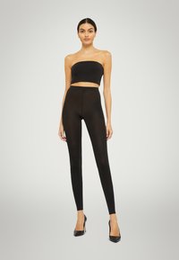 Zwarte gekorte strapless top en zwarte high-waisted leggings, beide aansluitend, gecombineerd met zwarte hoge hakken. Gladde textuur zonder zichtbare patronen.