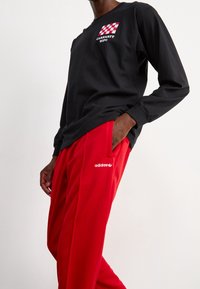 Svart långärmad tröja med röd och vit rutigt logotyp. Röda sweatpants med vit adidas-logotyp på vänster ben. Slät yta, avslappnad passform.