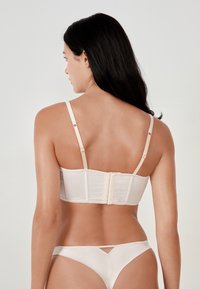 Light beige lingerie set featuring a bra with a structured back, adjustable straps, and a hook closure, complemented by matching bikini bottoms.