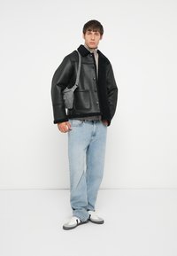 Schwarze Lederjacke mit einem Schafslederkragen, graue Umhängetasche, hellblaue Jeans und weiße Sneaker mit grauen Akzenten.