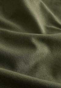 Primo piano di un tessuto verde oliva con una trama tessuta visibile e pieghe morbide che creano ombre delicate.