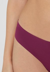 Bikini-Höschen in einem tiefen Beerenton, aus glattem Stoff, mit einem tief sitzenden Schnitt, minimaler Bedeckung und ohne sichtbare Hardware-Details.