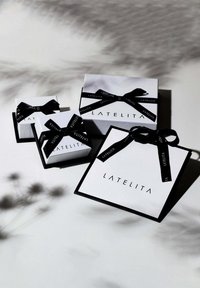 Three rectangular gift boxes in white, featuring black lids and black ribbons with "LATELITA" text. Distinct sizes arranged together.