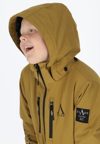 Khakifarbene Kapuzenjacke mit schwarzen Reißverschlüssen, Markenpatches und einer glatten Textur. Verfügt über einen hohen Kragen und verstellbare Kordeln.