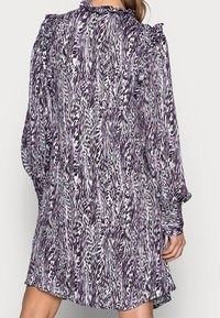 Fioletowo-biała sukienka w wzory z falbaniastym dekoltem i rękawami, charakteryzująca się luźnym krojem i fakturowanym materiałem. Krótka długość.