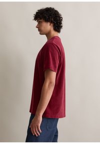 Burgundowa koszula z krótkim rękawem i okrągłym dekoltem, wykonana z miękkiego materiału bawełnianego. Prosty krój z luźnym dopasowaniem i bez widocznych wzorów.