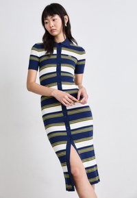 Adata polo kleita adītā ar jūras zilu, baltu un dzeltenu svītru rakstu. Tam ir īsas piedurknes, pogu aizdare priekšpusē un sānu šķeltne papildu detaļām.