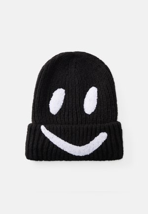 Zwarte gebreide beanie met een omslag, voorzien van een witte pluche smiley-gezichtsdesign. Ribbels in de textuur van de hoed voor extra warmte.