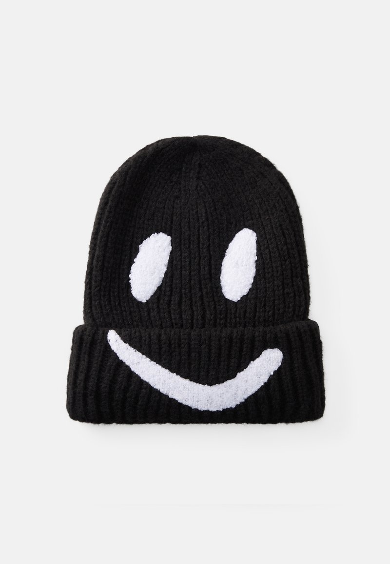 Zwarte gebreide beanie met een omslag, voorzien van een witte pluche smiley-gezichtsdesign. Ribbels in de textuur van de hoed voor extra warmte.