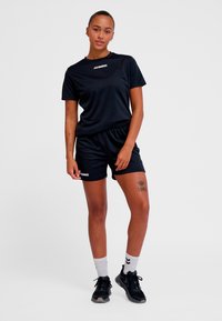 Ensemble sportif noir comprenant un t-shirt à manches courtes col rond et un short assorti. Fabriqué en tissu lisse et léger. Logo sur le devant.