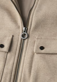 Béžová vlněná bunda se dvěma předními klopovými kapsami, černými patentkami a kovovým zipem s rytinou "Street One".