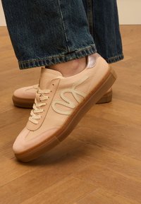 Leder-Sneaker in sanftem Rosa mit einer Wildlederspitze, einem beigen Logo und einem metallischen Fersenakzent. Verfügt über eine strukturierte Sohle und Schnürverschluss.