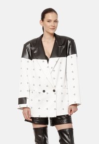 Dwurzędowa marynarka w białym i czarnym sztucznym skórze, z dużym kołnierzem, powtarzającym się czarnym wzorem logo oraz dwoma przednimi kieszeniami.