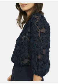 Marineblauwe doorschijnende blouse met gestructureerde bloemenborduursels, driekwartmouwen en een losse pasvorm. Zachte stof met gelaagde ontwerpdetails.