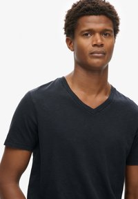 Camiseta de algodón negra de manga corta y cuello en V, con una textura suave, diseño ajustado y sin patrones ni logotipos visibles.