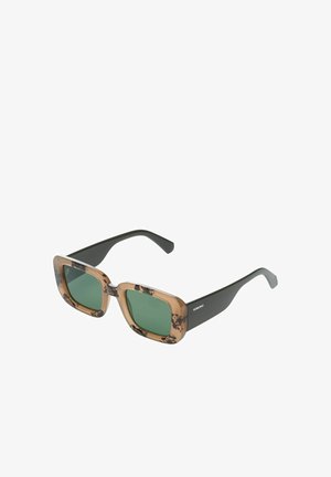 Lunettes de soleil carrées avec des verres verts, une monture avant en écailles de tortue, et des branches noires unies portant la marque Komono sur le côté.
