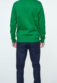 Zelená mikina vyrobená z bavlny, s dlouhými rukávy a vroubkovanými manžetami. V kombinaci s tmavě modrými džínami, které mají slim fit.