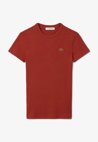 T-shirt en coton rouge à côtes, à manches courtes et col rond. Présente un petit logo de crocodile vert Lacoste sur la poitrine.