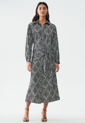 Vestido midi con estampado en blanco y negro, cuello camisero, mangas largas, detalle de cintura ajustable y falda acampanada.