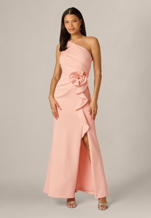 Kobieta w różowej sukni do ziemi z jednym odsłoniętym ramieniem, dużym kwiatowym detalem i rozcięciem z przodu, nosząca wiszące kolczyki i srebrne szpilki.