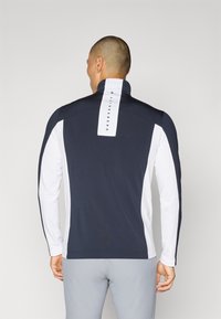Men’s long-sleeve athletic top in navy and white. Features a high collar and a vertical brand logo on the back. Smooth texture, fitted design.