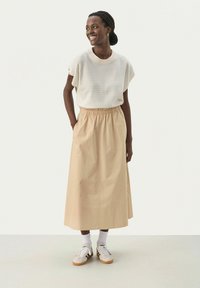 Beige midi skirt with elastic waistband, paired with a white striped short-sleeve top. Worn with white sneakers and light socks.