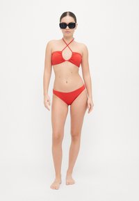 Piros bikini szett, amely halter nyakú toppal rendelkezik, kulcslyuk kivágással és állítható pántokkal, párosítva a hozzá illő, alacsony derekú alsó résszel. Simaság jellemzi.