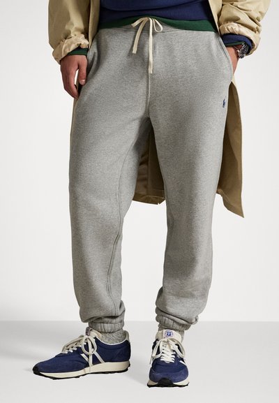 Grijze jersey sweatpants met een elastische tailleband en boorden, voorzien van zijzakken en een klein blauw logo. Gecombineerd met blauwe hardloopschoenen.