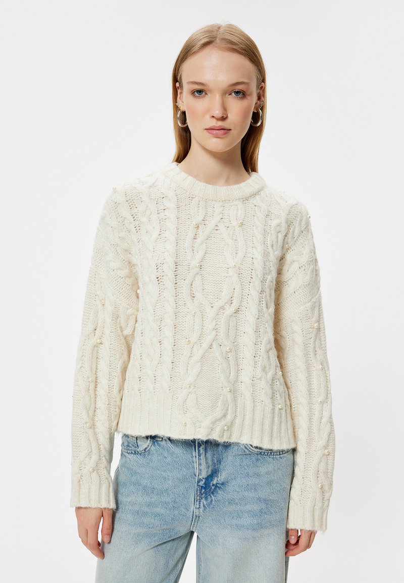 Chunky-Cream-Kabelstrickpullover mit geripptem Saum und Bündchen, der dekorative Perlenakzente im gesamten strukturierten Design aufweist.