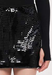 Fustă mini neagră din sequins, cu sequins dreptunghiulari care creează o suprafață strălucitoare și texturată, având un talie ajustată și un material superior neted.