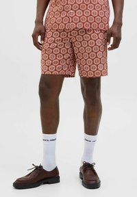 Crvene šortse sa uzorkom i bijelim cvjetnim dizajnom, uparene s smešnim cipelama i bijelim čarapama sa oznakom "JACK & JONES."