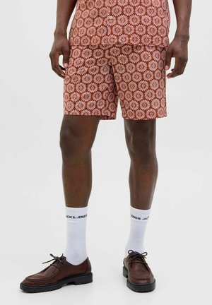 Crvene šortse sa uzorkom i bijelim cvjetnim dizajnom, uparene s smešnim cipelama i bijelim čarapama sa oznakom "JACK & JONES."