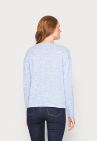 Sweater azul claro com uma textura suave, corte relaxado, ombros caídos e detalhes em canelado. Combinado com jeans de denim escuro.
