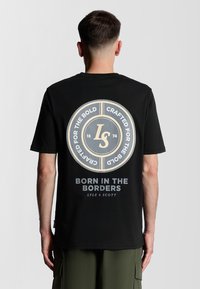 T-shirt noir à manches courtes avec un grand graphique rond au dos, comportant du texte et un logo de marque dans des tons beiges et gris. Tissu en coton.