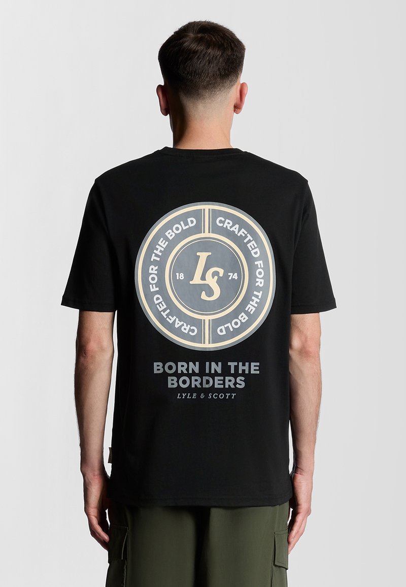 T-shirt noir à manches courtes avec un grand graphique rond au dos, comportant du texte et un logo de marque dans des tons beiges et gris. Tissu en coton.
